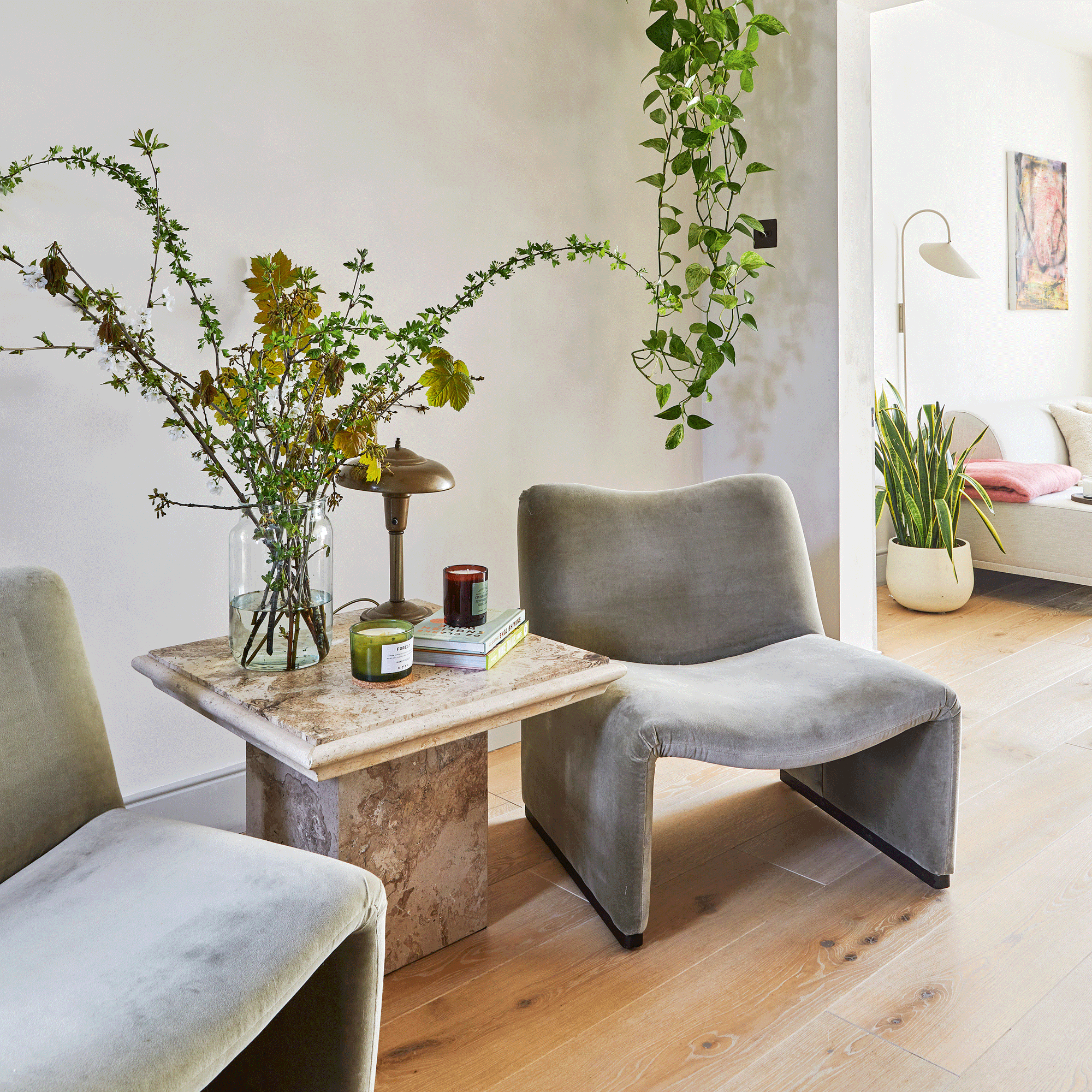 a seating area with two grey occasional chairs and a marble side table with flowers and trailing houseplants