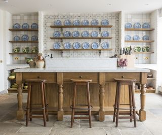 wooden kitchen island with seating and marble worktop in front of blue and white china plate displays