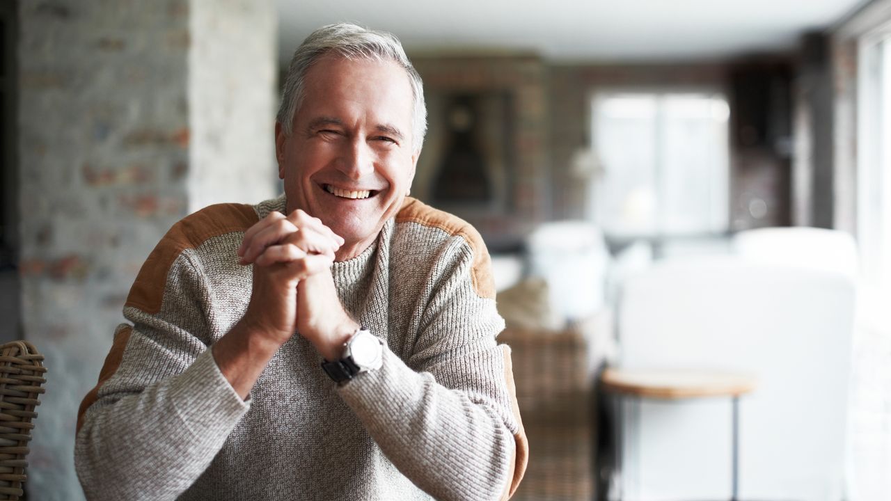 Older white male sitting on a kitchen table smiling