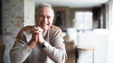 Older white male sitting on a kitchen table smiling