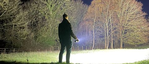 A person with their back to the camera shining the Acebeam X75 across a field and into woodland
