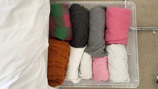 Under bed sweater storage in a clear container showing multi-colored sweaters.