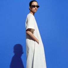 Woman wearing sunglasses and white long dress in front of blue background