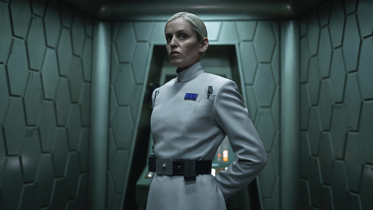 Still from the Star Wars TV show Andor. Denise Gough returns as Dedra Meero. She is a stern looking woman with slicked back blonde hair and is wearing a white uniform.