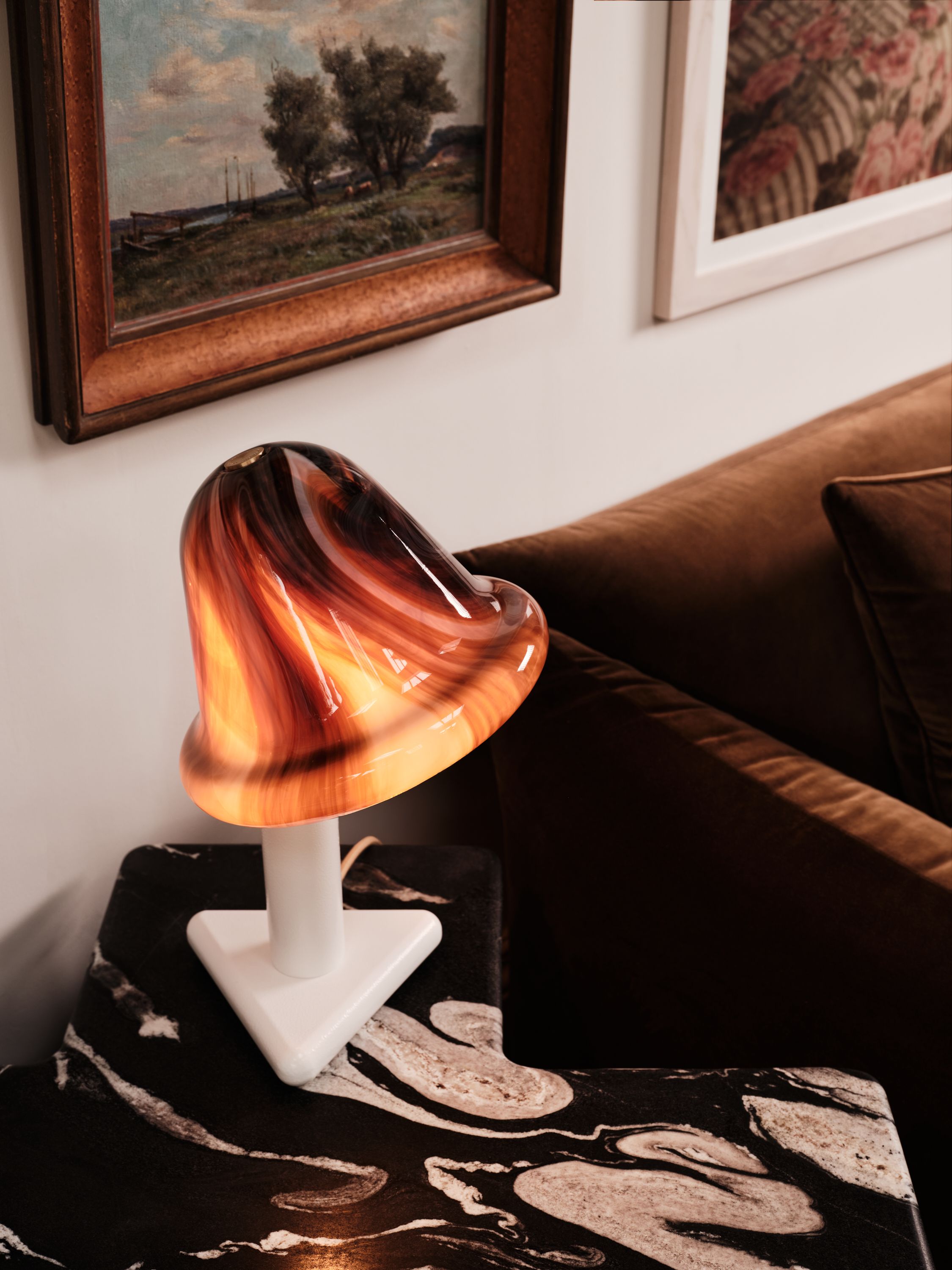 a marble brown table lamp on a patterned table with traditional art in the background