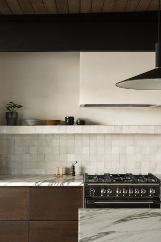 A kitchen with zellige tiles, wooden cabinetry, and a marbe countertop