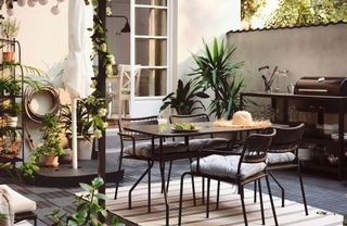 Black metal dining table and dining chairs in an outside space, rug on floor, lots of potted plants