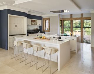 white kitchen double islands with stone flooring, bar stools, navy wall