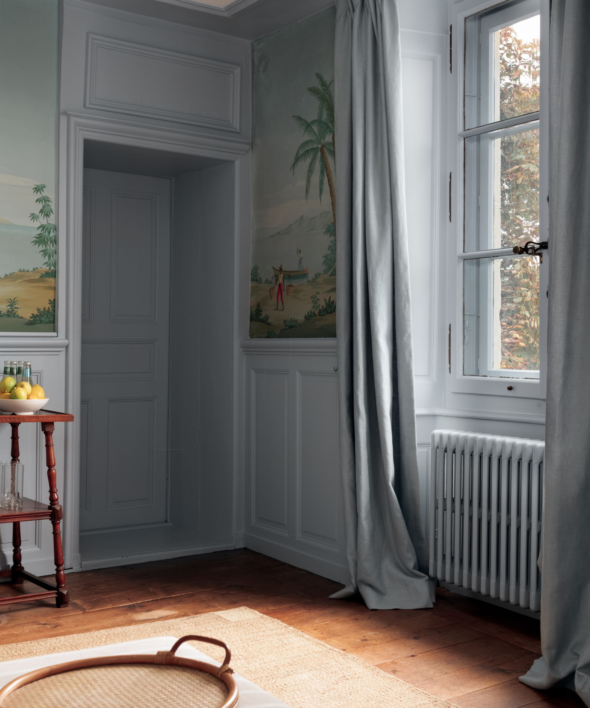 A pale blue living room with a landscape wall mural.