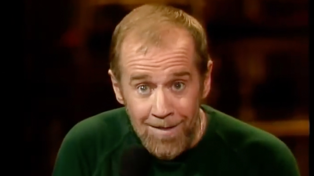 George Carlin performing, in a green shirt, making a silly face in one of his 12 HBO specials.