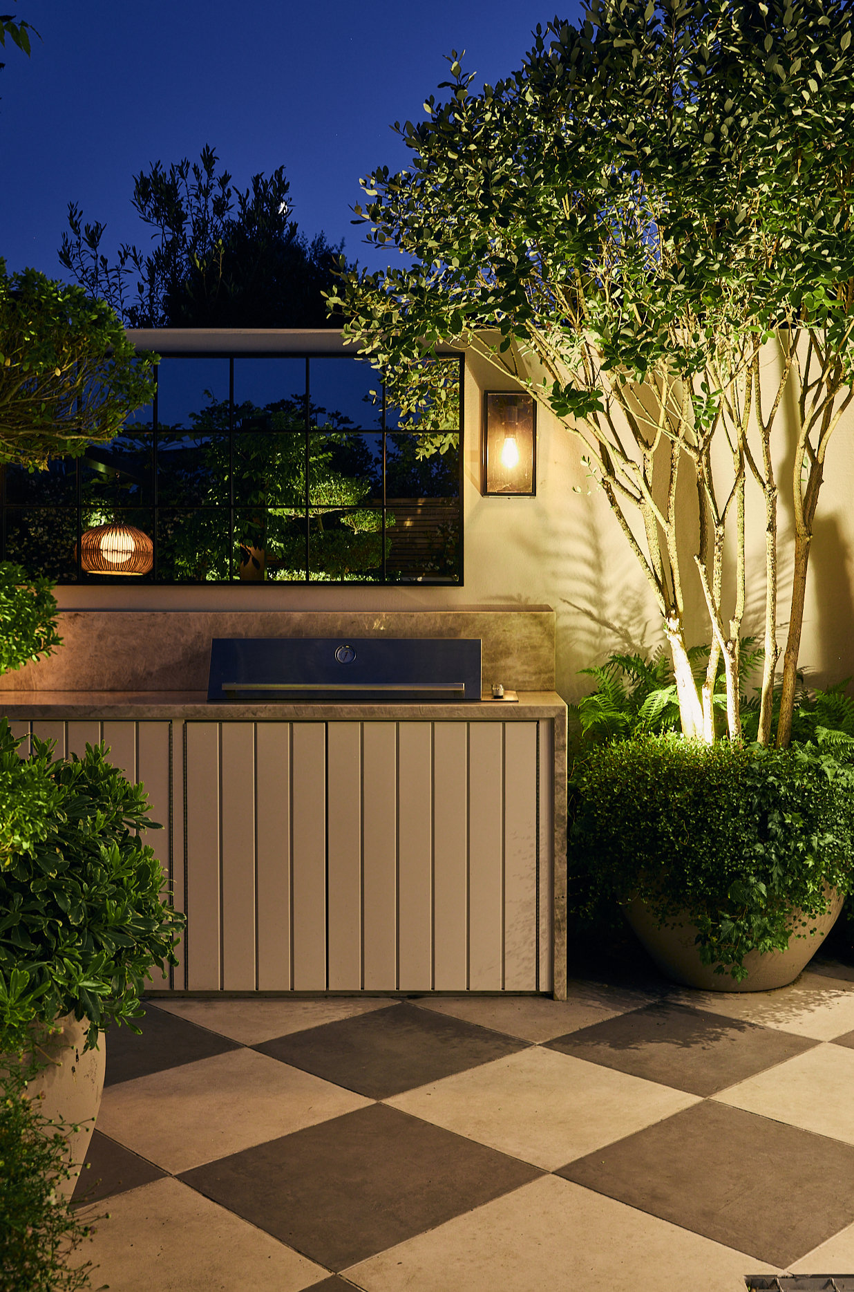patio with large checkerboard tiles and outdoor kitchen illuminated at night