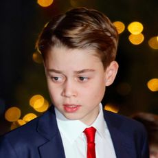 Prince George wears a navy suit, white shirt, and red tie