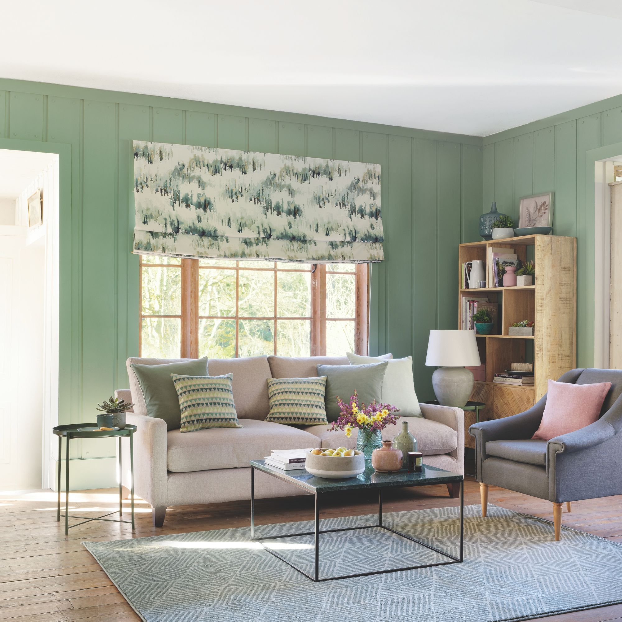 A living room with green panelled walls, a beige sofa with green cushions and a geometric rug on the floor