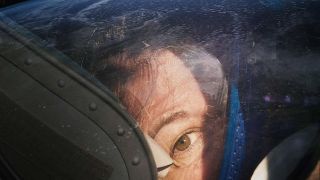 a person's eye can be seen looking through the glass of a spacesuit helmet. stars can be seen filling the background
