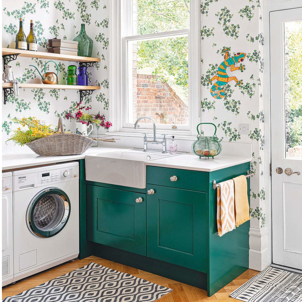 kitchen with green cabinets, white washing machine, white sink and green and patterned wallpaper with wooden shelving