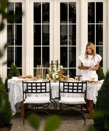 An outdoor lifestyle photograph of interior designer Shea McGee seated at a beautifully set dining table in a lush garden setting.
