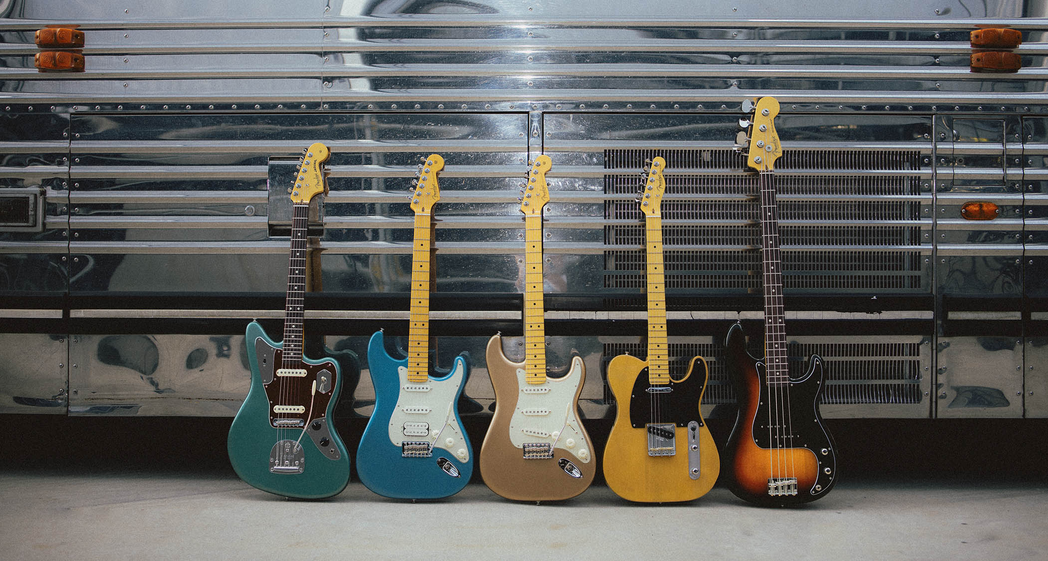 Fender&#039;s American Professional Classic series photographed against the side of a chrome tour bus [L-R]: Jaguar in faded Sherwood Green Metallic, HSS Stratocaster in Faded Lake Placid Blue, Stratocaster in Faded Firemist Gold, Telecaster in Faded Butterscotch Blonde, Precision Bass in Faded 3-Color Sunburst.