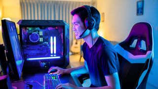 A PC gamer sitting at a desk wearing a headset with purple-blow LED lighting.