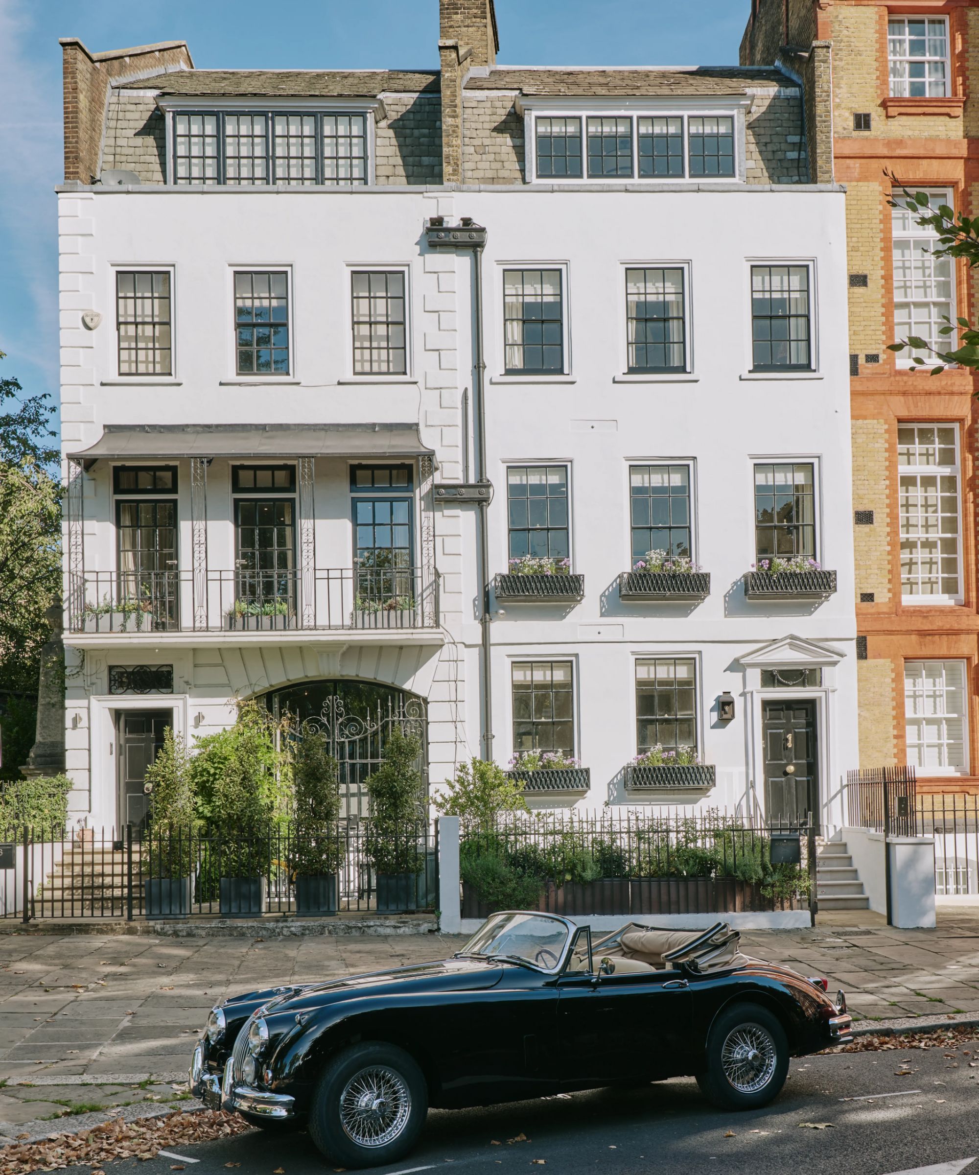 a white painted georgian townhouse in london with original windows and window boxes and a vintage car parked out the front