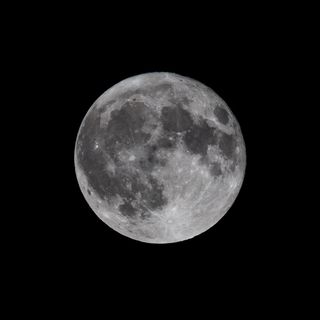 A fully illuminated moon against a black backdrop of night sky.