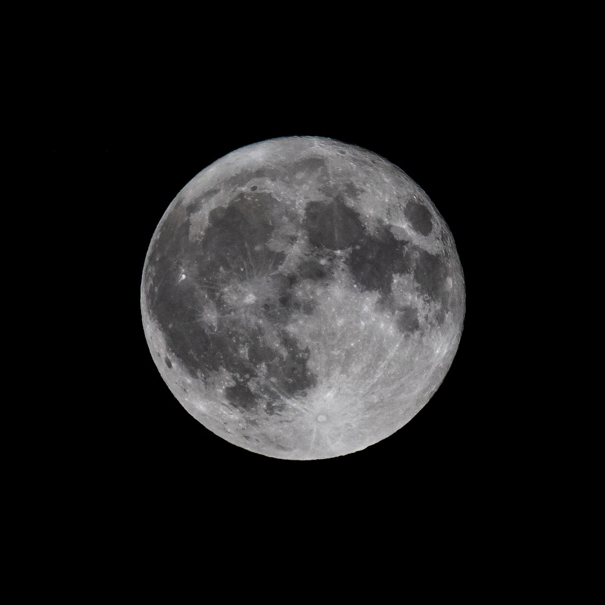 A fully illuminated moon against the black background of the night sky.