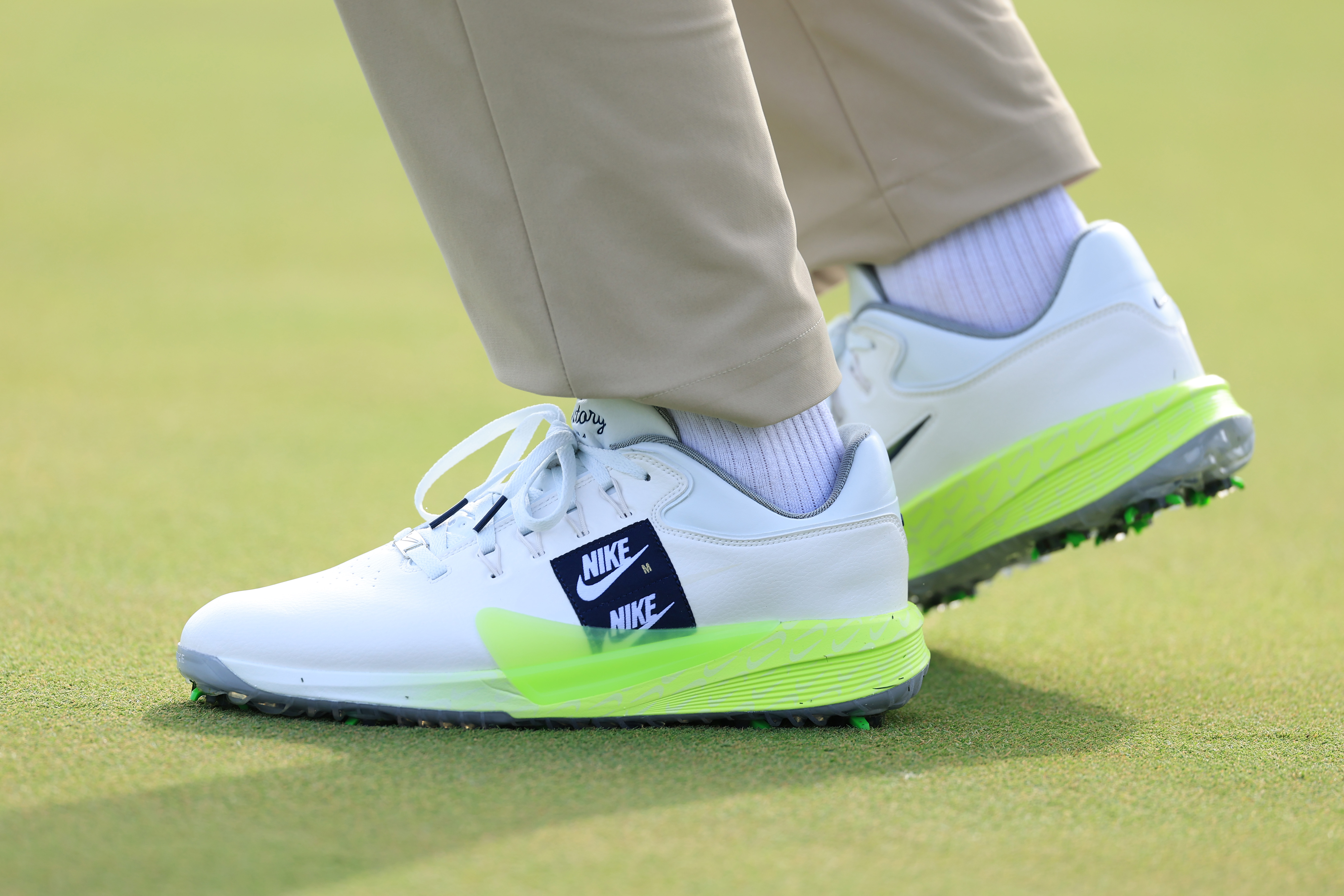 A pair of white Nike Golf shoes showing a double Nike logo