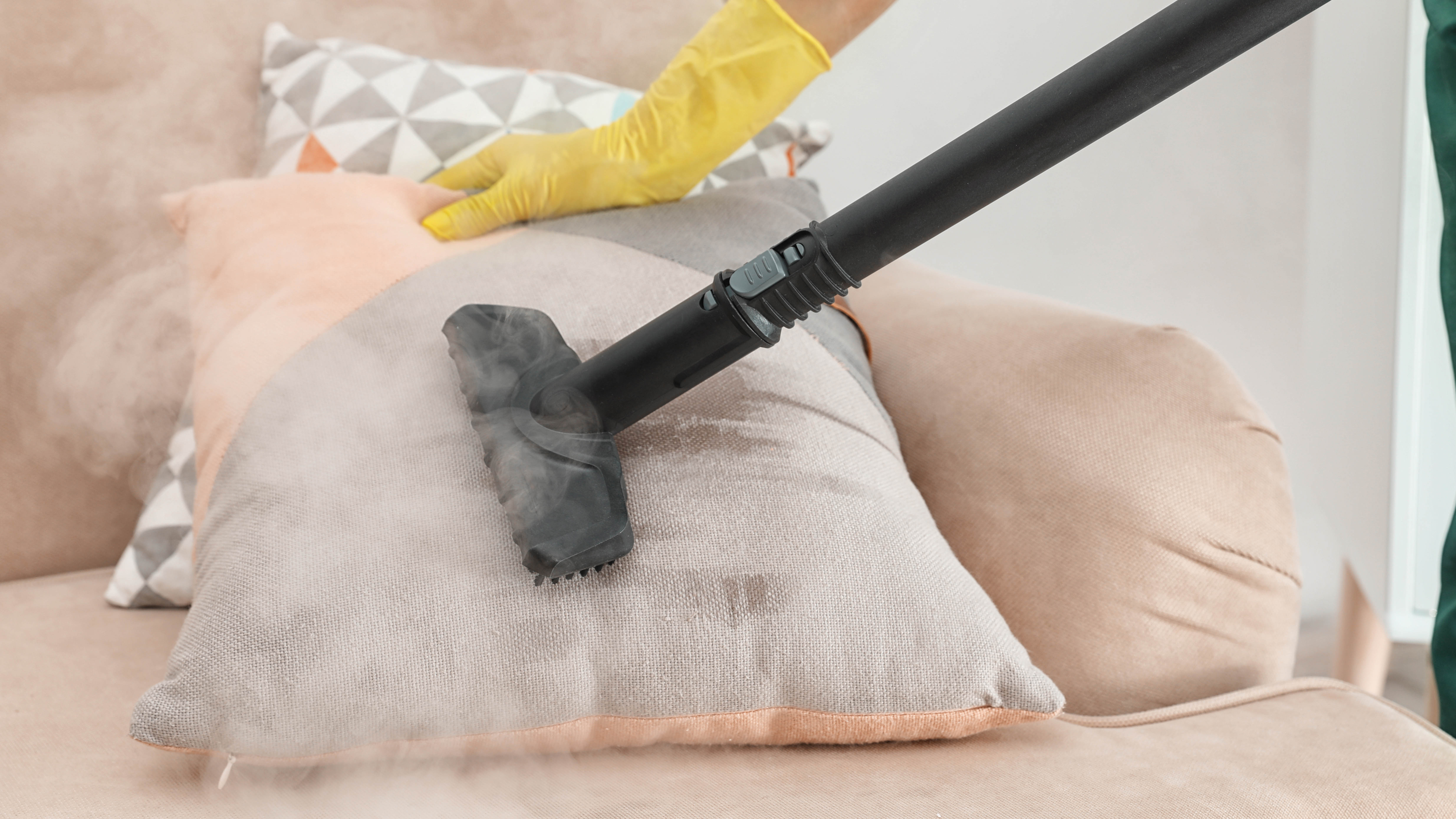 Someone using a steam cleaner on a couch cushion