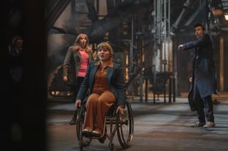 Shirley Anne Bingham (Ruth Madeley) positions her wheelchair at a door ready to fire weapons while Sylvia (Jacqueline King), Donna (Catherine Tate) and the Doctor (David Tennant) stand back