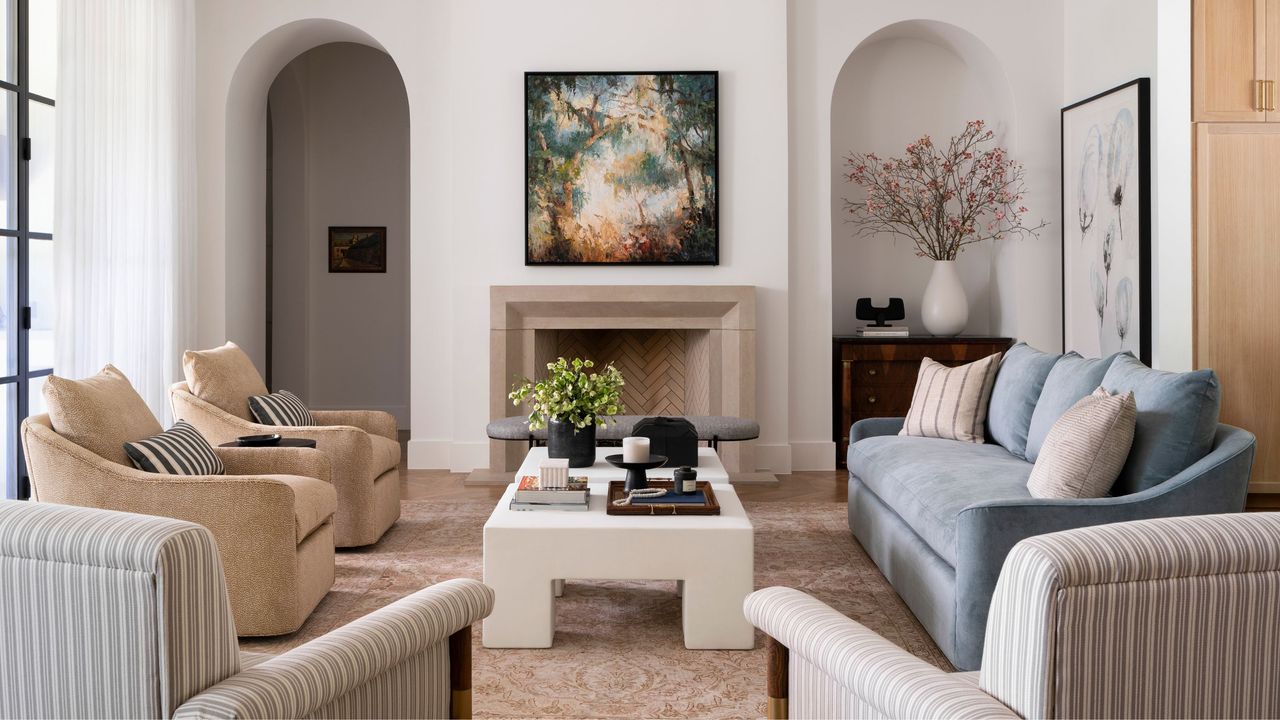 formal living room with blue sofa, two brown armchairs, and two striped armchairs in front of a white coffee table and marble fireplace