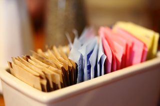 Close-Up Of Sugar And Sweetener Packets In Container At Cafe.