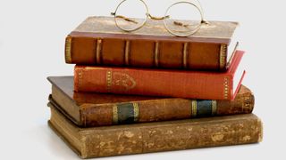 A stack of old books topped with a pair of glasses