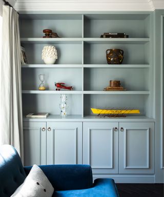 Living room detail with fitted light blue-gray cabinet in alcove, each shelf decorated with colorful objects and accessories.