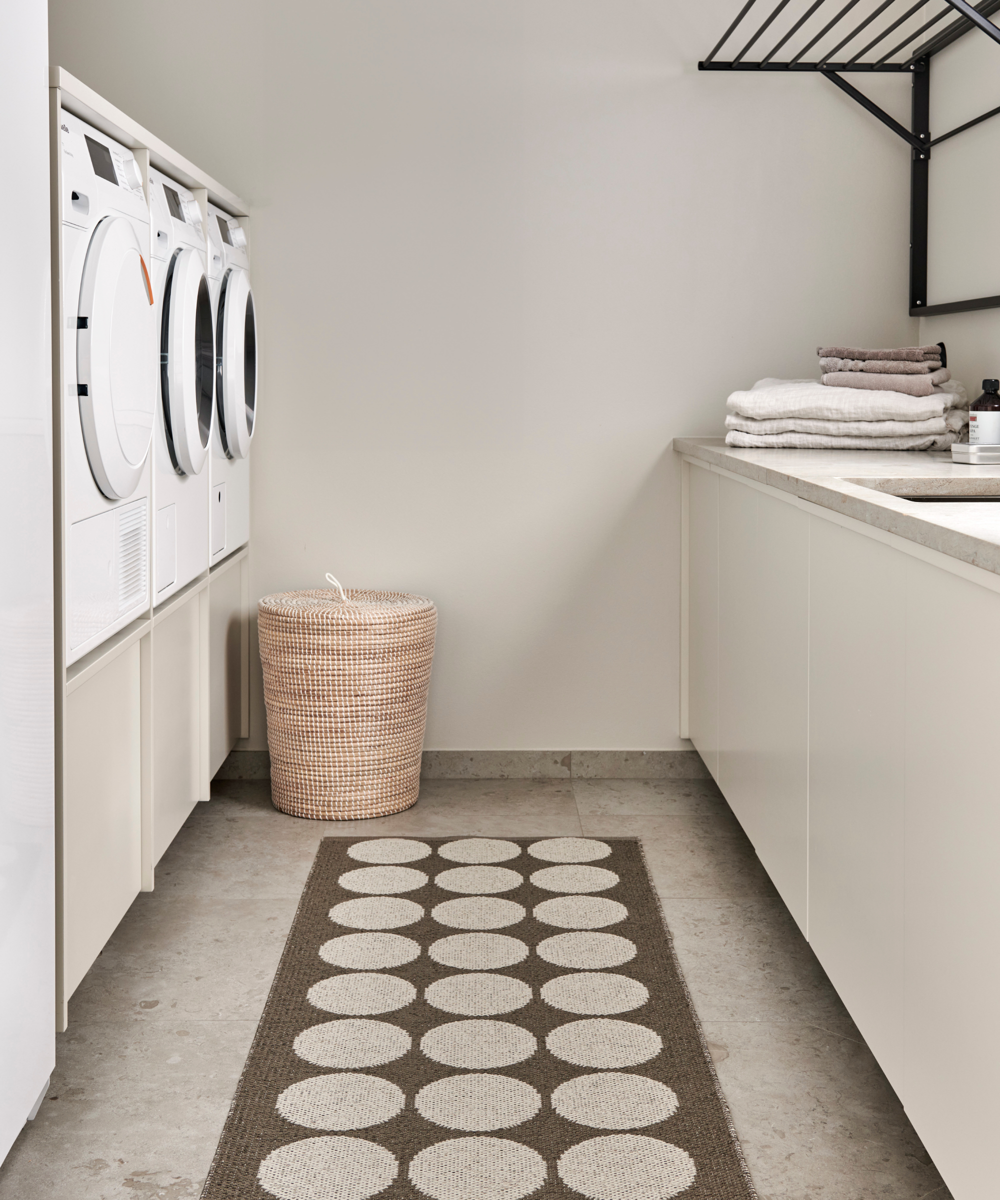 narrow utility room with appliances on one side of room, worktop and storage with drying rack on wall on the other