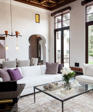 A living room with a white sofa, a glass coffee table, and high, detailed ceilings