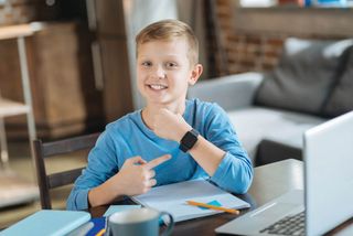 Delighted boy smiles while pointing at his smartwatch