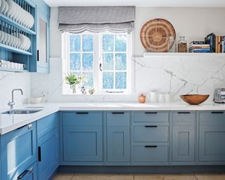 Blue painted kitchen cabinetry with white marble backsplash and wall decor.