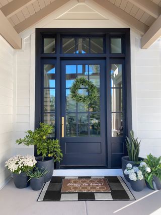 A front porch with a door with a green leaf and a patterned dormat