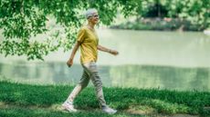 older woman walking on grass with a body of water behind her