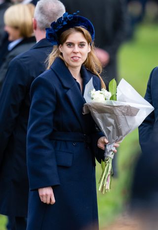 Princess Beatrice wearing a blue coat and holding flowers