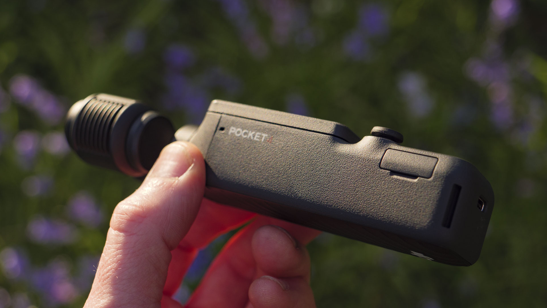 Side profile of the DJI Osmo Pocket 4 vlogging camera with natural background of bluebells