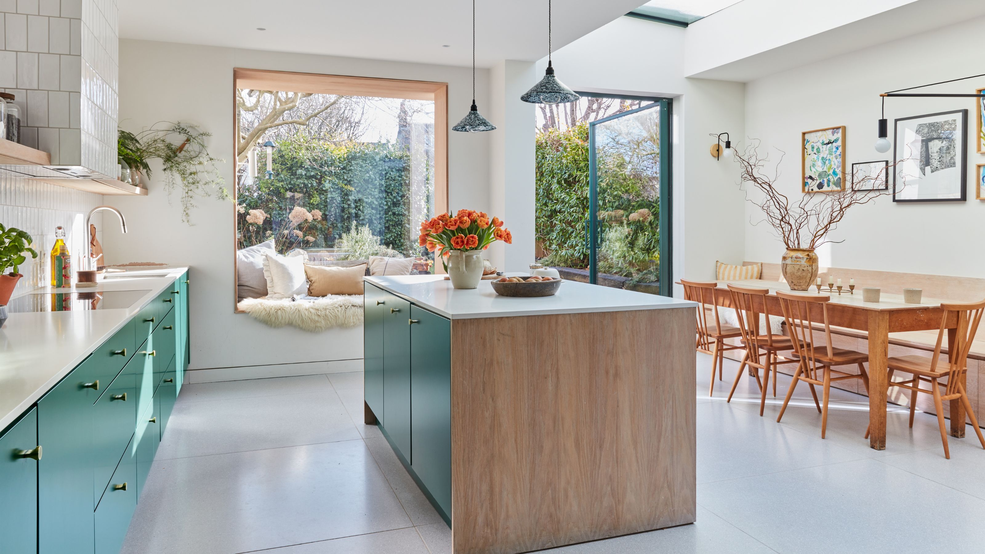 White kitchen with a dining table on the right and an island in the middle and a window seat behind it