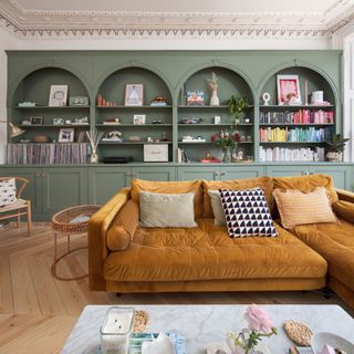 A living room with a built-in arched bookcase and a velvet chaise sofa in ochre