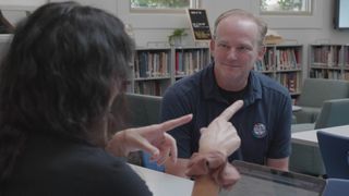 Michael Morrison talks with a fellow educator. They are both seated at the table.