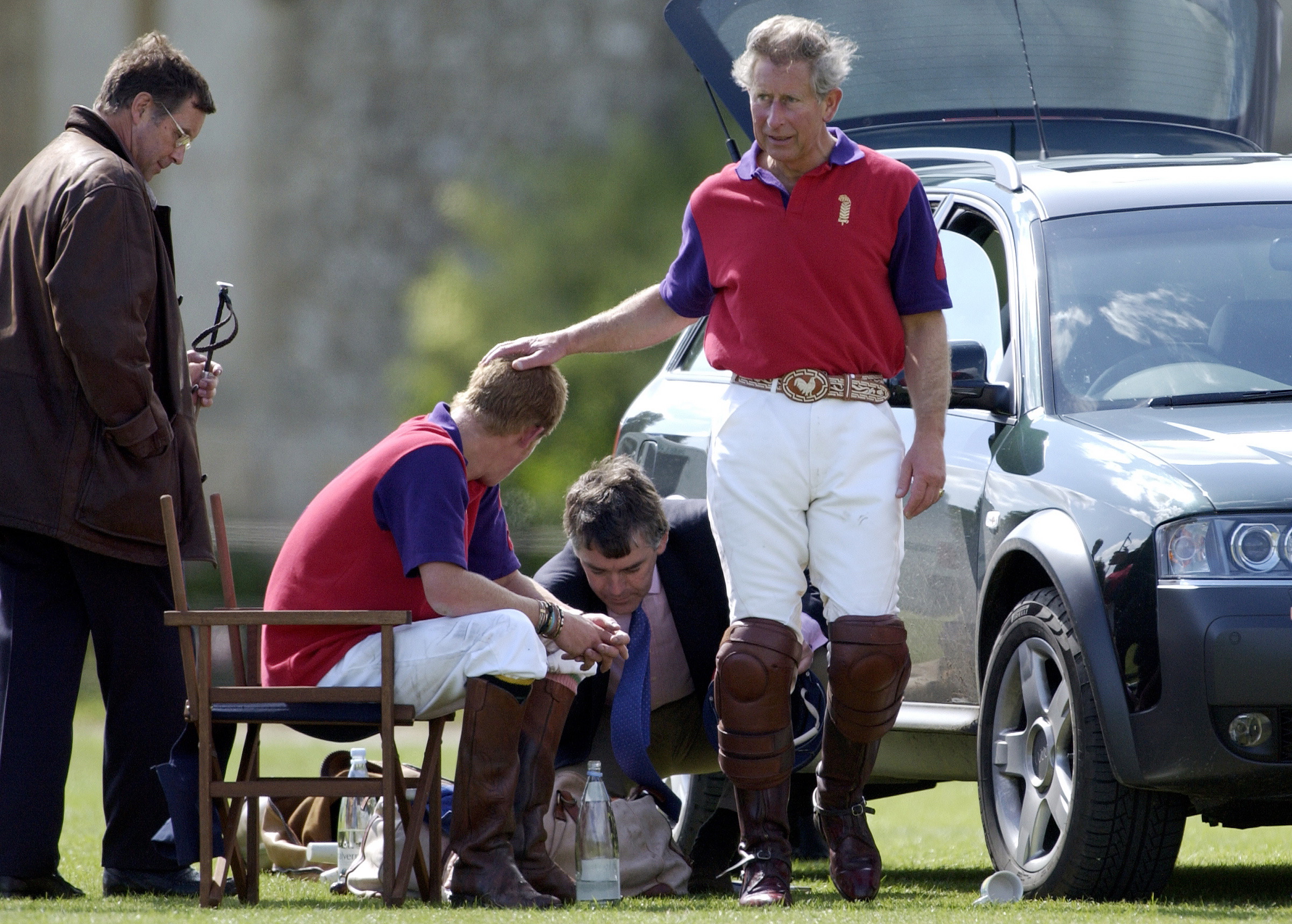 Prince Harry and King Charles wear red and purple polo shirts while interacting at a polo match in July 2004 at Cirencester Park Polo Club.