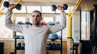 Man performs dumbbell shoulder press in gym