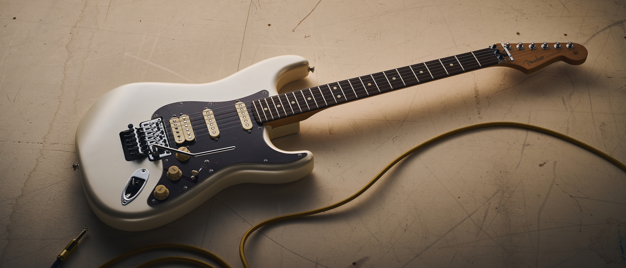 A Fender Player II Modified Stratocaster HSS Floyd Rose lying on a concrete floor with a guitar cable