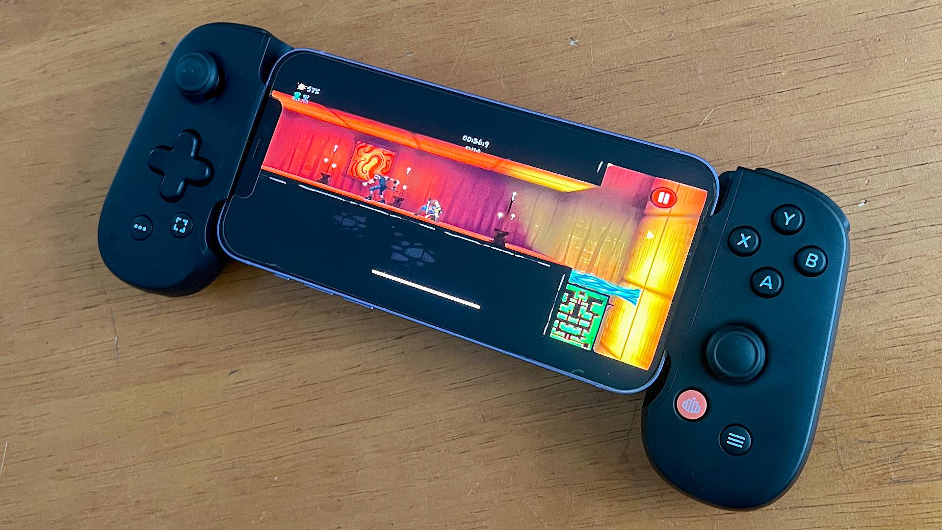 iPhone connected to Backbone One controller on wood desk.