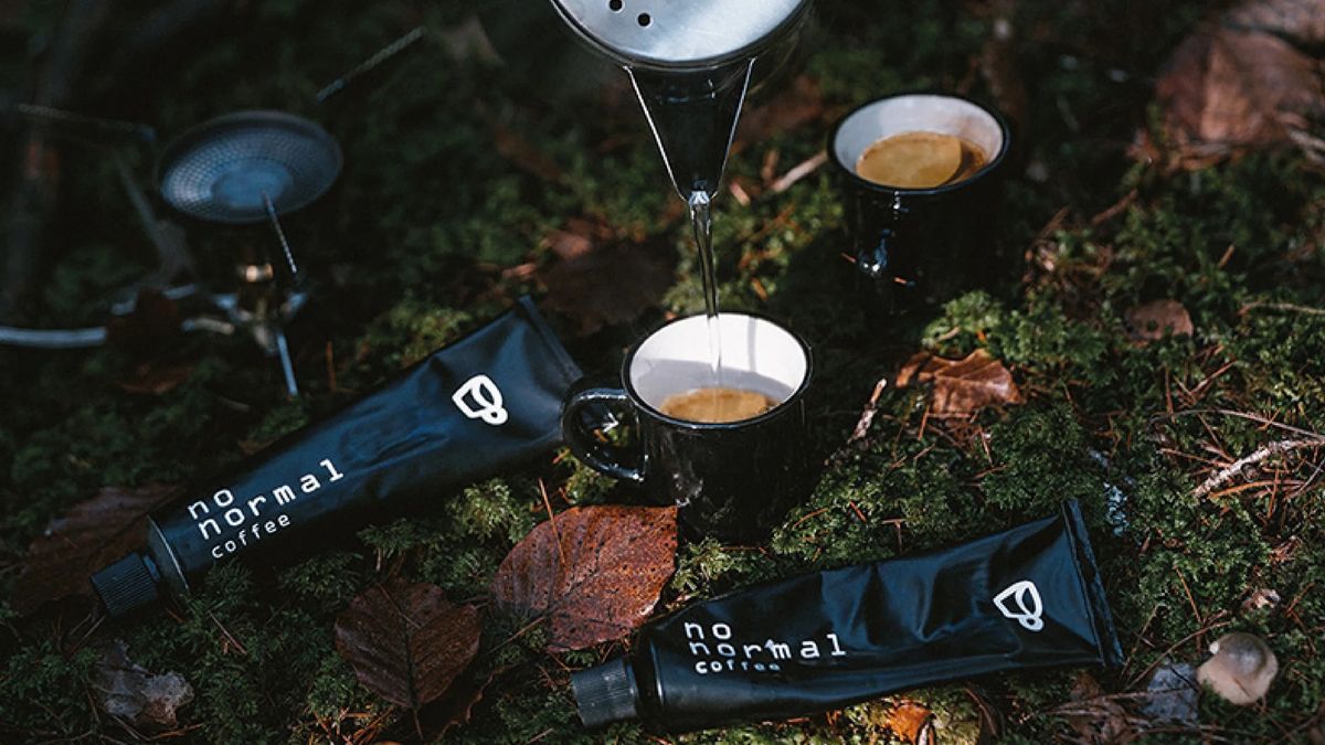 Two cups of coffee and two tubes of No Normal coffee paste on forest floor