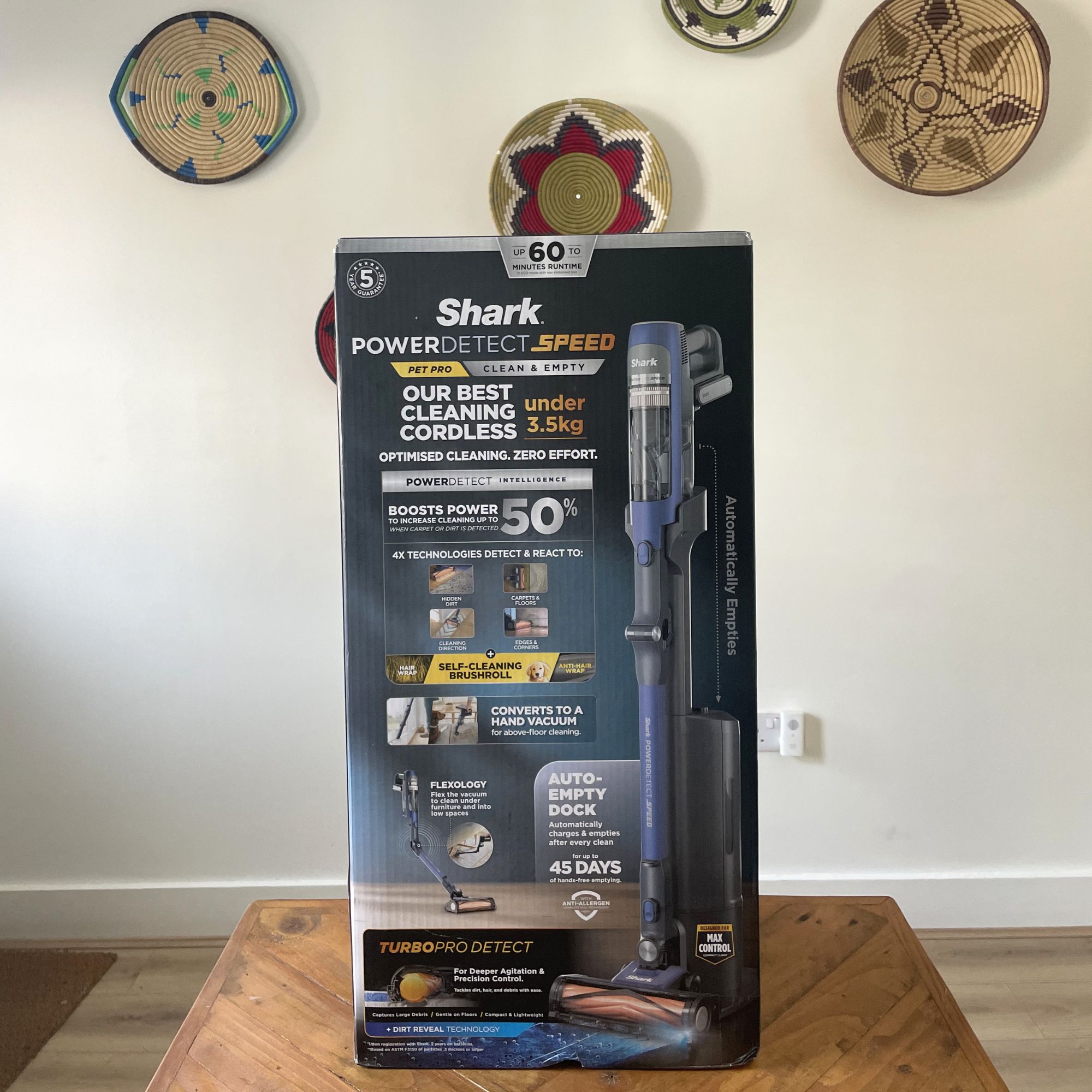 Box of a shark vacuum cleaner on a wood table in front of a white painted wall