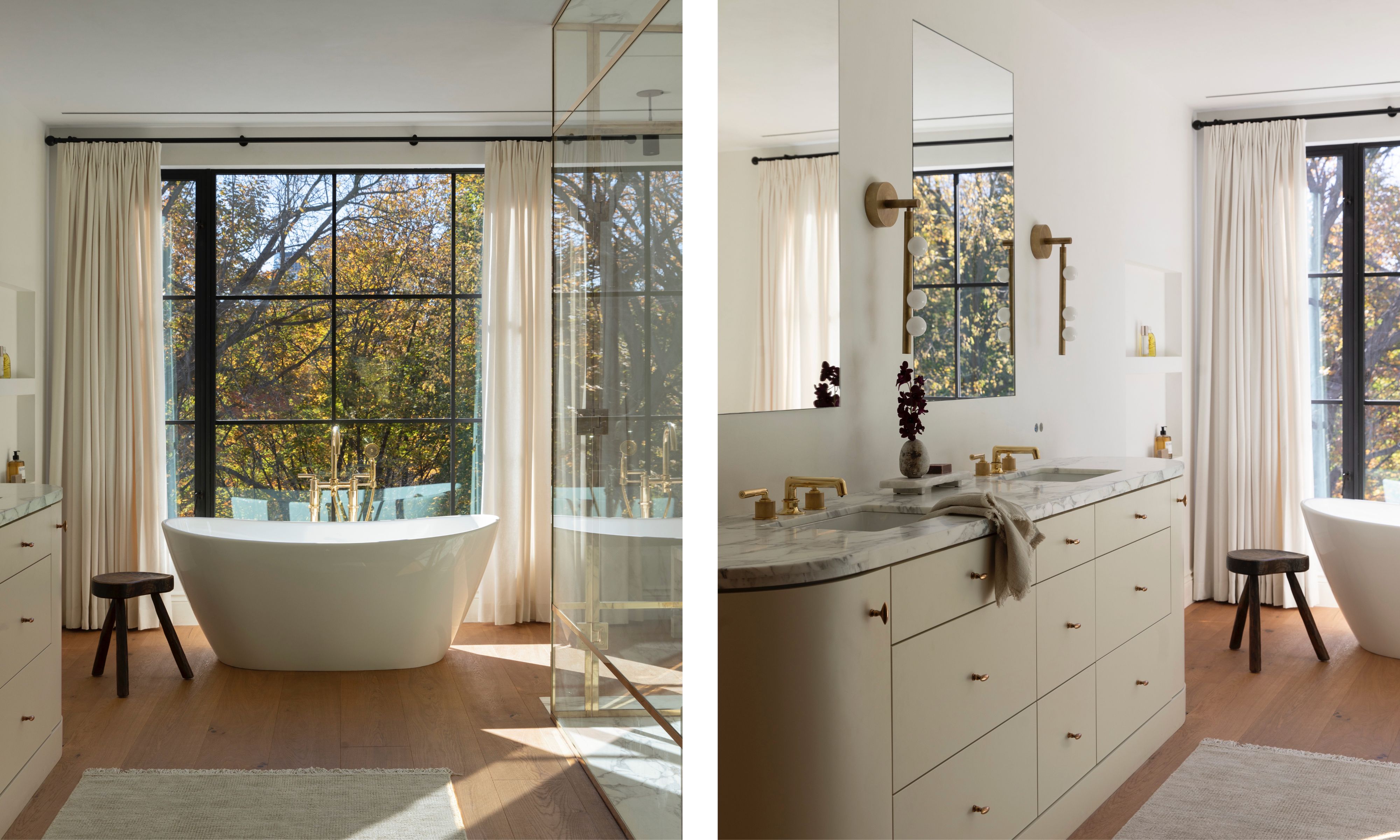 A split-view image of a sun-drenched primary bathroom. The left side features a freestanding white soaking tub with gold fixtures positioned in front of a large black-framed window showcasing autumn trees. The right side shows a wide cream vanity with a marble countertop, double sinks, and elegant gold wall sconces, reflecting a clean and modern luxury aesthetic